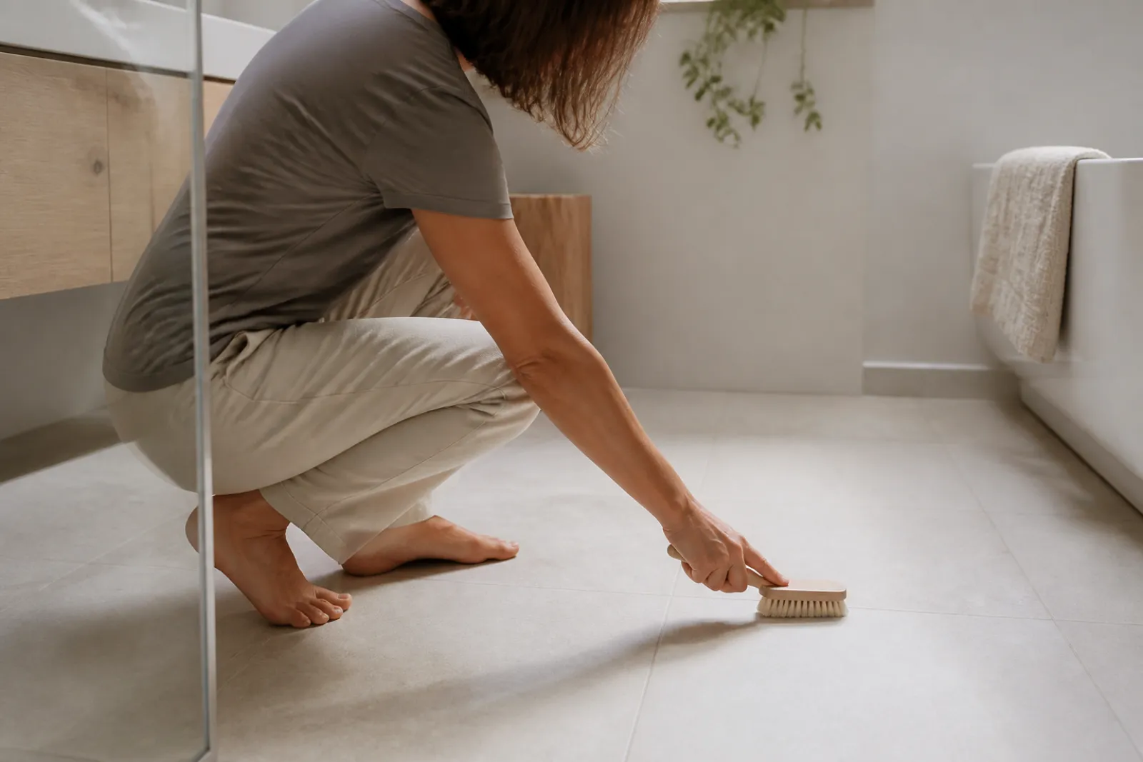 Person kneeling to inspect grout lines on a bathroom floor